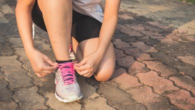 woman lacing up her gray and pink nike low top athletic shoe